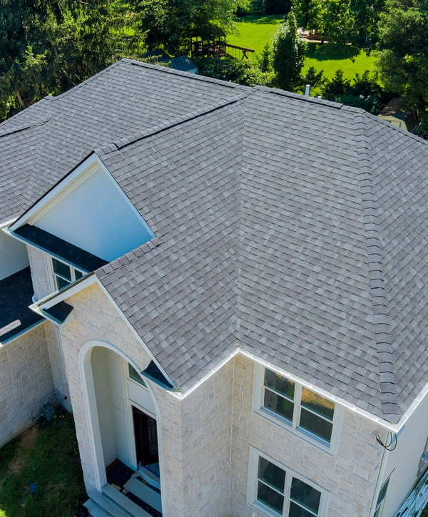 Aerial drone shot of a large suburban home featuring a complete roof replacement with light grey architectural shingles.