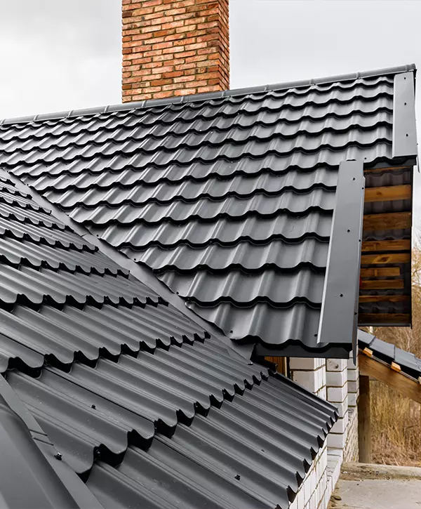 Close-up of a newly installed black metal tile roof showing the flashing detail around a red brick chimney.
