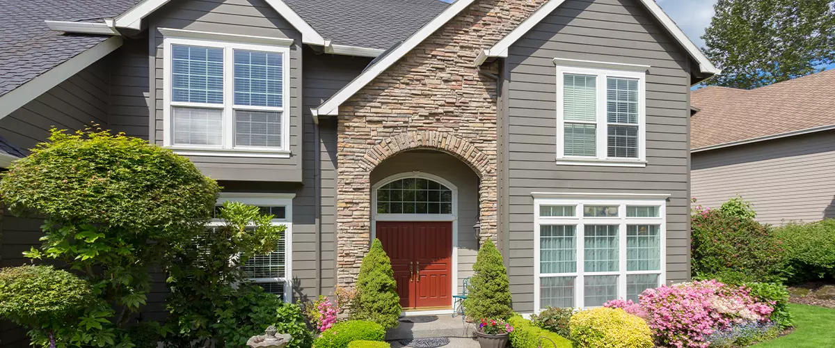 Grey horizontal exterior cladding paired with a rustic stone entryway arch and bright red front doors.