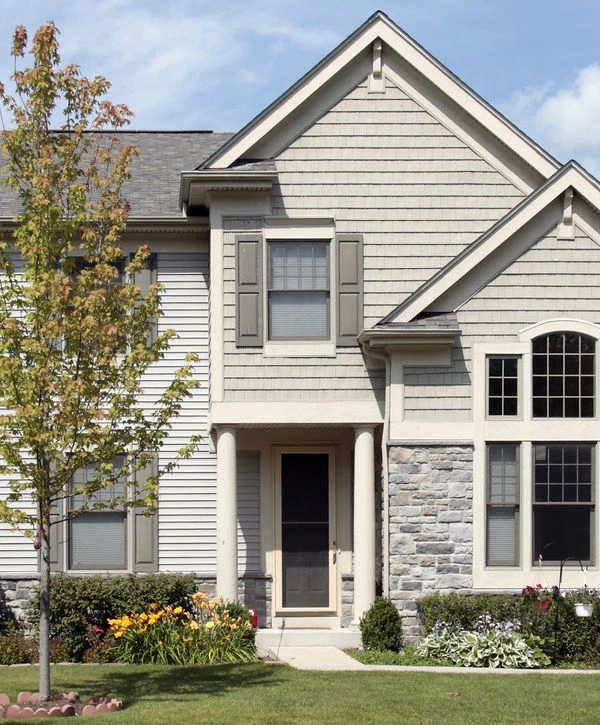 Front elevation of a house showcasing a combination of light grey shake siding and stone veneer accent walls near the columned entryway.