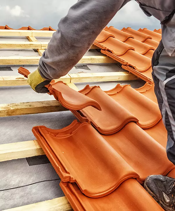 Professional contractor installing orange clay roofing tiles on wooden battens, showing the detailed process of new tile roof installation for maximum weather protection.