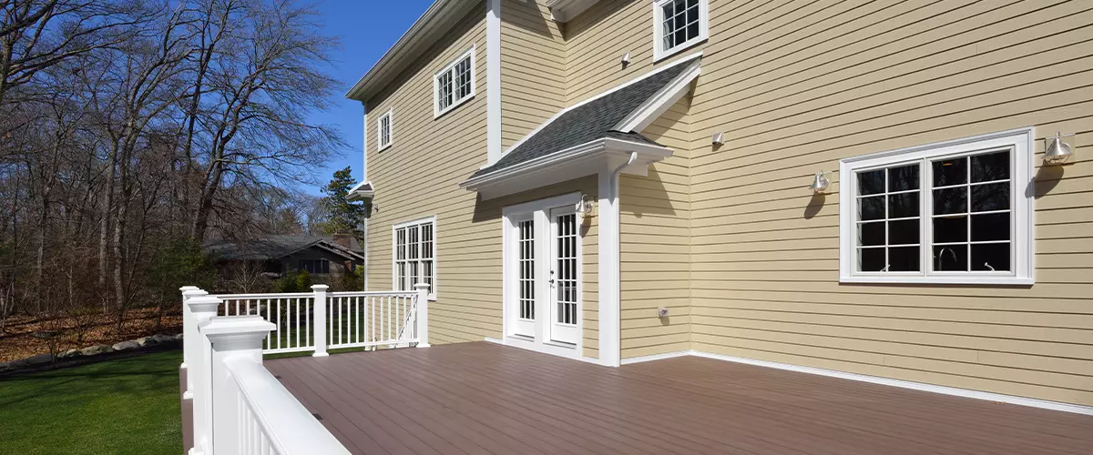Backyard view showing a home with yellow horizontal clapboard siding, white French doors, and a spacious brown composite deck with white railings.