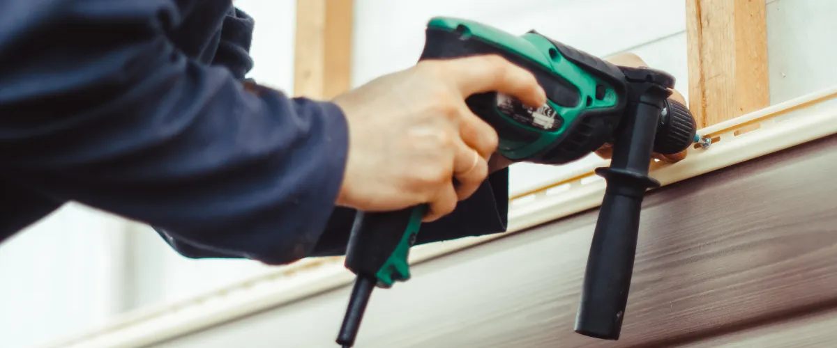 a person using a power drill during the installation of vinyl siding on a building