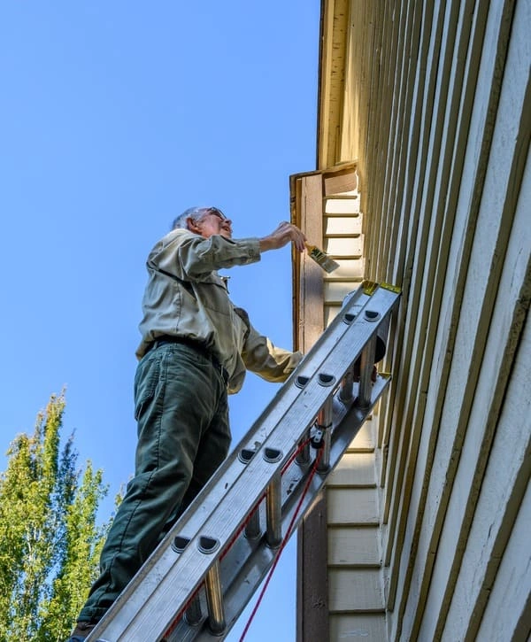 A contractor standing on an extension ladder to paint and finish a siding repair project for a home in Holmdel, NJ.
