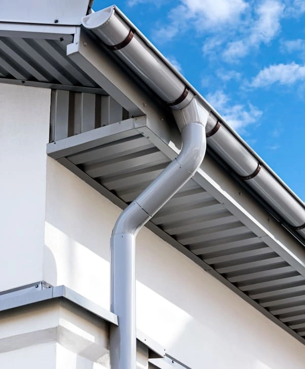 A close-up view of a newly installed, modern white seamless gutter and downpipe system on a residential home during a professional gutter installation in Holmdel, NJ.