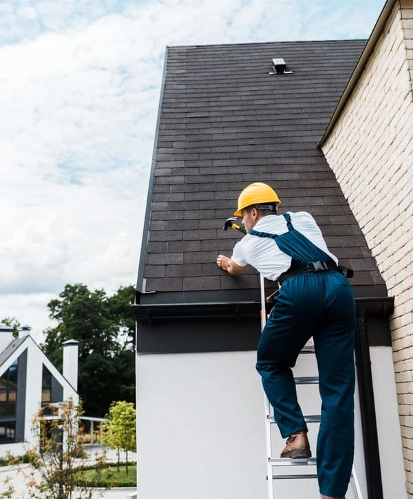 A professional roofer in a yellow hard hat standing on a ladder while performing a precision roof repair in Colts Neck, NJ.