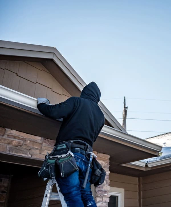 Close-up view of a skilled installer working on a residential gutter replacement in Holmdel, NJ, secured on a ladder against a tan siding house.