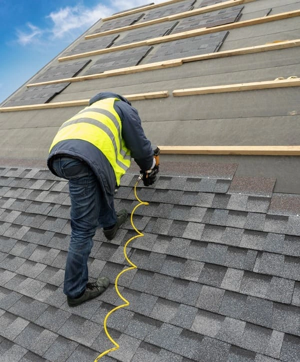 A roofing contractor in a safety vest performing a roof installation in Holmdel, NJ, using a nail gun to secure architectural shingles.