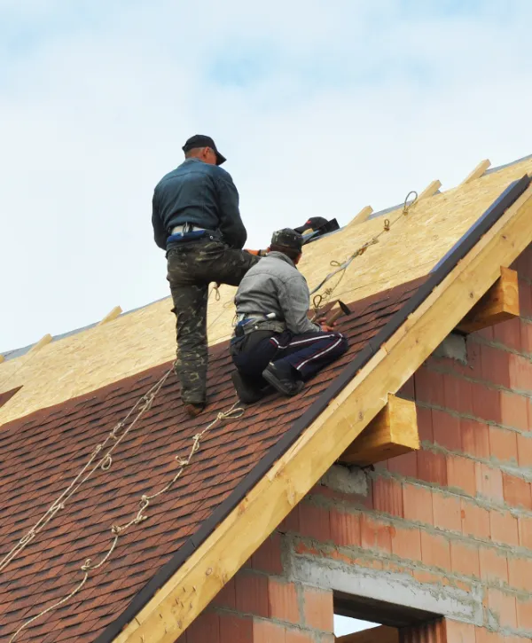 two construction workers installing asphalt shingles on the roof of a new house