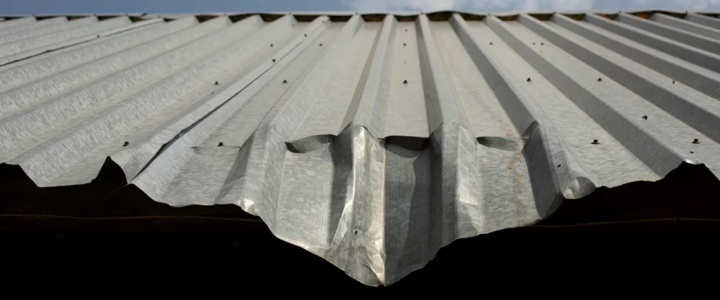 Perspective view of a corrugated metal roof featuring visible hail damage and deep indentations along the ridges.