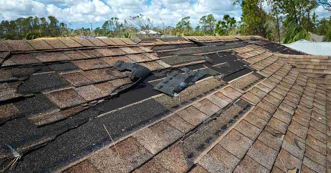 A wide view of extensive roof damages with missing shingles and exposed underlayment under a cloudy sky.