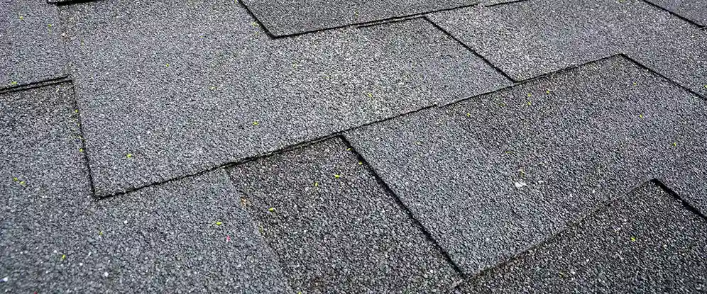 Detailed close-up of durable dark grey asphalt shingles on a suburban house roof.