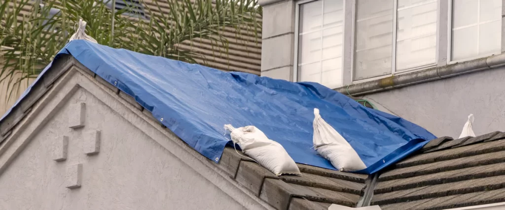 A blue heavy-duty tarp secured over a damaged roof section for temporary protection.