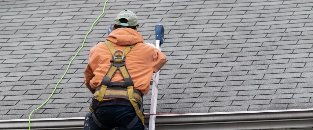 A professional roofing contractor in safety gear inspecting shingle integrity.