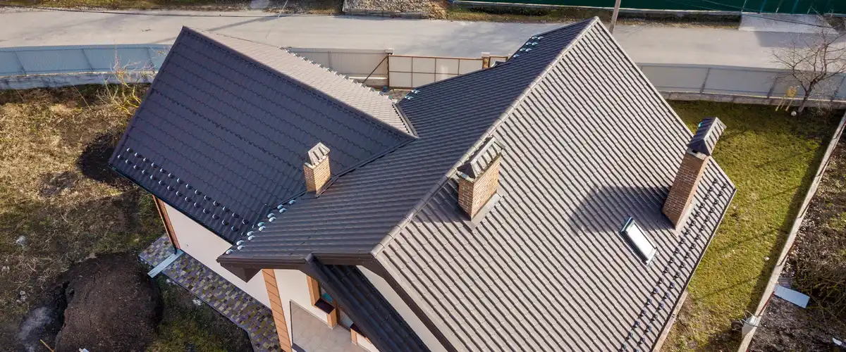 High-angle aerial shot of a large family home showcasing a dark brown multi-gabled metal roof with brick chimneys and integrated skylights.