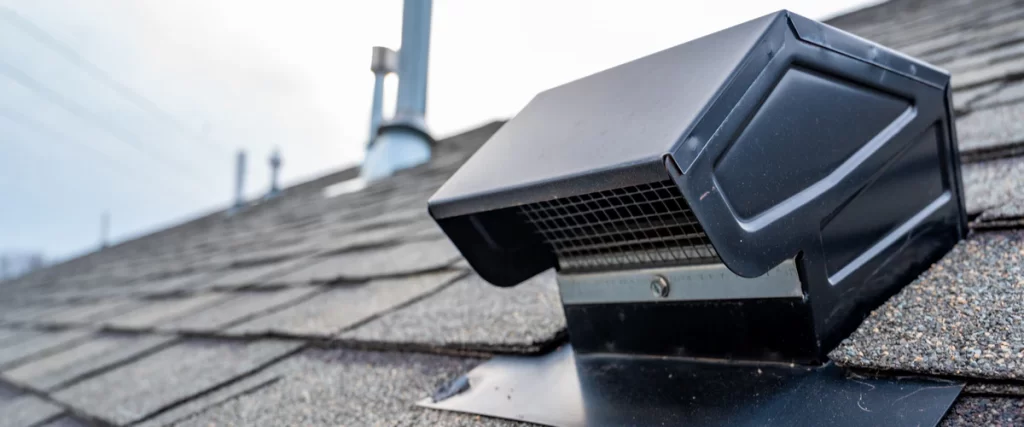 A black metal box-style roof vent installed on an asphalt shingle roof, highlighting the type of external exhaust needed to prevent poor attic ventilation.