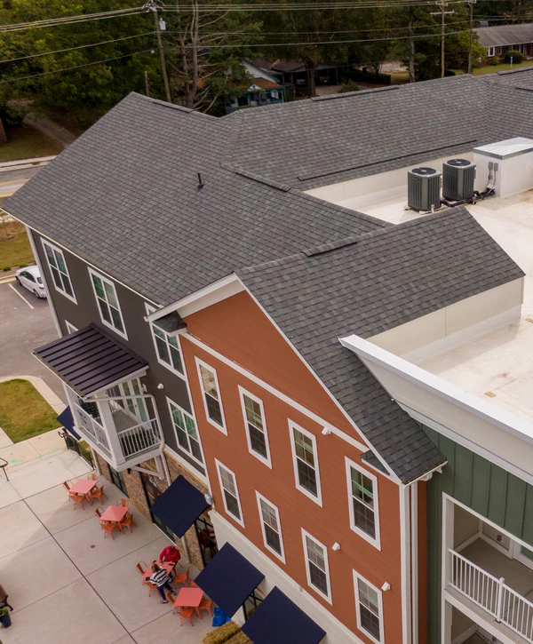 Aerial view of a multi-colored mixed-use building in New Jersey featuring newly installed grey ashpalt shingle roofing, black window awnings, and an outdoor patio seating area.