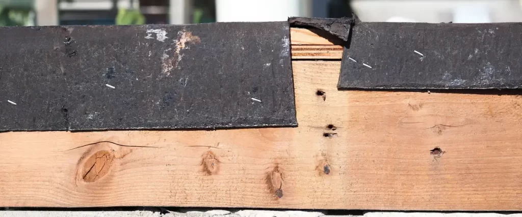 Close up of an unfinished or damaged roof edge demonstrating flashing failures, where the black protective barrier is torn and inadequately nailed to the exposed wood.