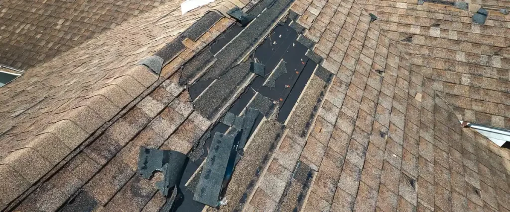 A large vertical section of a residential roof showing missing and severely damaged shingles, leaving the dark protective underlayment completely exposed to the elements.