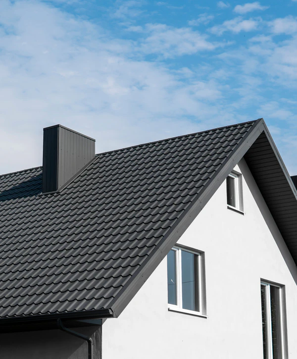 Close-up of a modern white residential home featuring a durable charcoal black metal roofing system and matching metal chimney.