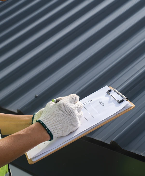 Close-up of a contractor's gloved hands filling out a checklist on a clipboard during a metal roof inspection in New Jersey.