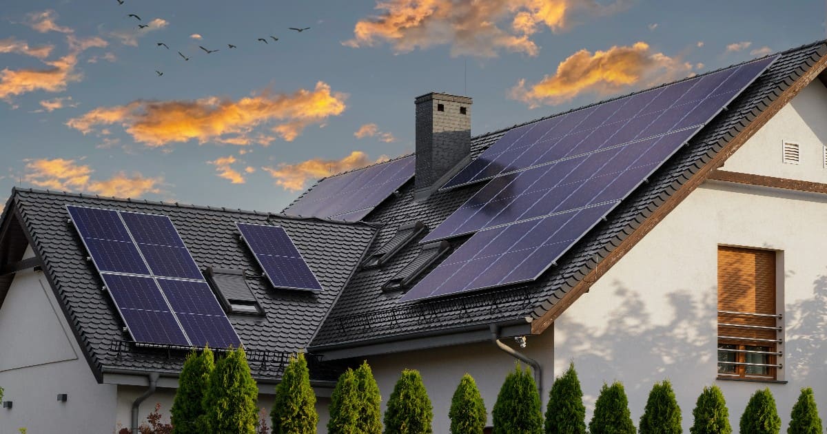 A white house with a dark shingled roof featuring multiple solar arrays at sunset, illustrating a proper installation to avoid a roof leak under solar panels.