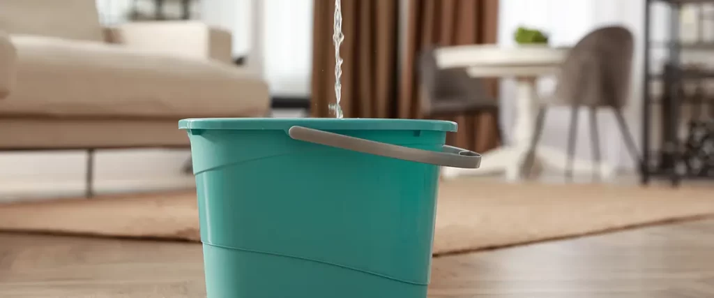 Bucket collecting water from a roof leak inside a home to prevent floor water damage