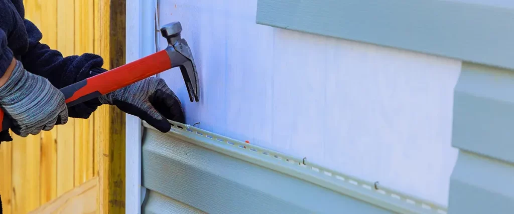 Close-up of vinyl siding installation with hammer during residential exterior renovation and siding replacement