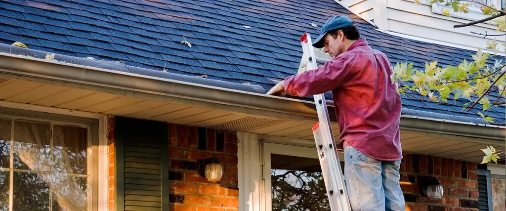 Professional performing gutter cleaning on a residential home using a ladder to remove roof debris