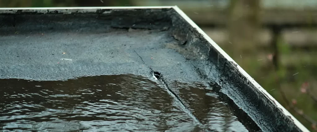 Standing water on a flat roof caused by drainage issues and potential roof leak damage