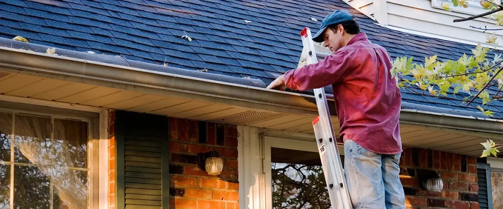 Technician installing gutter guards and cleaning roof gutters on a residential home exterior