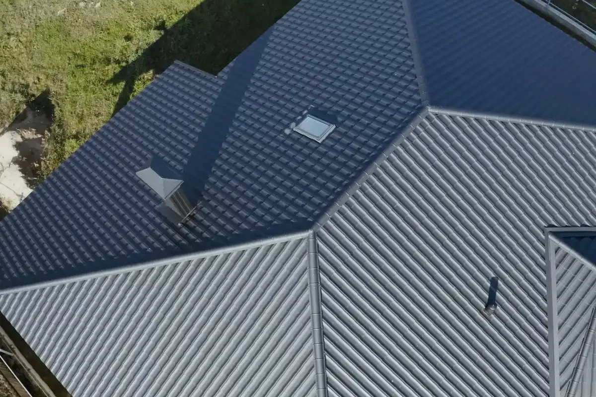 An aerial view of a complex dark grey metal roofing system with a tile profile, featuring a skylight and chimney on a residential house.