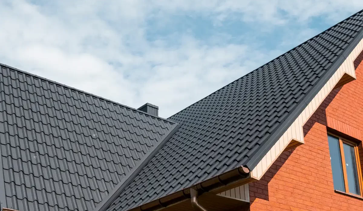 A close-up of a black wave-profile metal roofing system on a red brick house, showing the valley transition and brown guttering.
